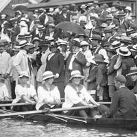 Image: A large crowd watches four female rowers and their male cox 