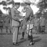 Image: Two men in military uniforms shake hands on an open field. A group of Australian Army soldiers stand in a line in the background