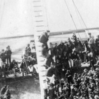 Image: A large crowd of men gather on a wharf to hear a speech