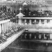 Image: A crowd of people in early twentieth century attire are gathered at the side of a large swimming pool