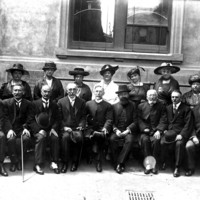 Image: Group of men and women sit and stand in two lines, most wearing dark clothing and hats