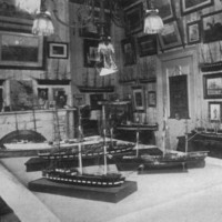 Image: A small room festooned with several works of art on its walls and ship models on tables