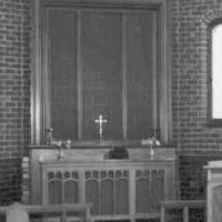 Image: The interior of a Christian chapel constructed from brick. It is an austere structure that features two lines of simple wooden pews and a small wooden altar
