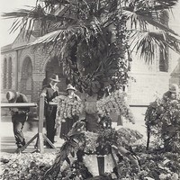 Image: Floral tributes rest against a large palm tree
