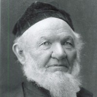Image: a head and shoulders portrait of a man with a bushy white beard wearing a dark velvet cap.