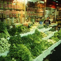Image: woman standing with large display of vegetables in front of Asian grocery store