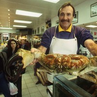 Image: man holding large crab in front of him with people looking on