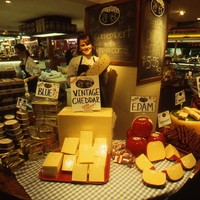 Image: woman standing surrounded by cheese in market stall