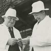 Image: Two men in white coats and hats smiling and engaging in conversation
