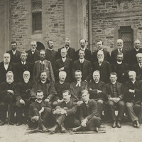 Image: A group portrait of ministers in front of a stone church. There are four rows, two standing, two sitting of 28 people.