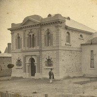 Image: Two large interconnected synagogue buildings, a man stands in the bare yard at the front of the building. 