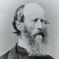 Image: a head and shoulders portrait of a man in three quarter profile. He is balding but has a long bushy beard. 