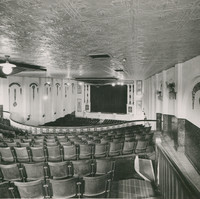 Image: Inside of a theatre hall, view of a front stage overlooking rows of chairs and a balcony