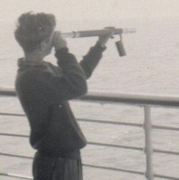 Image: boy holding telescope and looking out over ocean