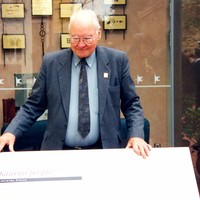 Image: elderly man standing behind large graphic plaque