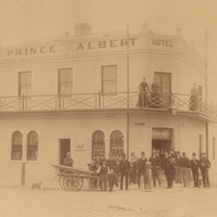 Image: A group of men standing in front of the Prince Albert Hotel. Three women are standing on the balcony.