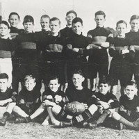 Image: a group of boys in football uniforms with their teacher. The boy seated in the centre of the front row holds a football with 