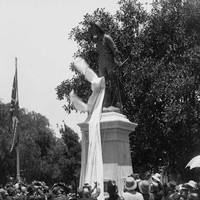 Image: crowd of people surrounding large bronze statue with cloth being removed. 