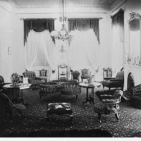 Image: A drawing room of a large house with high ceilings, a fireplace and a number of chairs scattered around the room