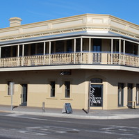 Image: A cream-coloured two-storey building with upstairs verandah. A sign over the front door reads ‘McGrath’s British Hotel’