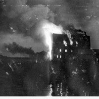 Image: A large, multi-storey building is completely consumed by fire. The blaze is taking place at night, and in close proximity to a river