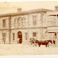 Image: A horse-drawn cart parked in front of three bluestone buildings. 