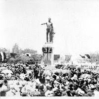 Image: crowd of people around bronze statue of man pointing