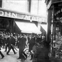 Image: crowds of people, dressed fairly formally, in front of shop awnings