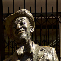 Image: bronze statue of smiling man leaning back with hands in pockets