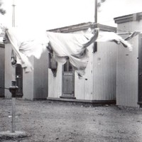 Image: clothesline in front of small, corregated iron buildings.