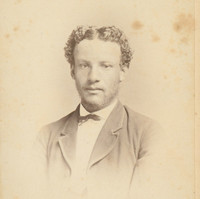 Image: Photographic portrait of a man with wispy stubble and short slightly curly hair. He is wearing a suit jacket, shirt and small bow tie.