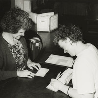 Image: two smiling caucasian women writing at a main desk in library