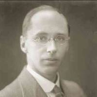 Image: A photographic head-and-shoulders portrait of a young, clean-shaven Caucasian man wearing an early-20th century suit and wire-rimmed spectacles