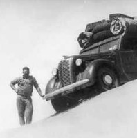 Image: Man stands leaning on heavily loaded truck perched on top of a sandhill