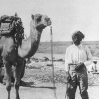 Image: Man in turban standing with saddled camel