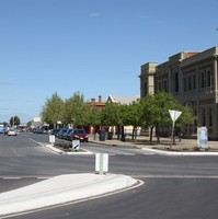 A large wide street in foreground extends into the distance. There is a large white stone building on the right hand corner