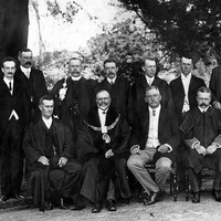 Image: A group of men in Edwardian attire pose for a photograph. One of the men is wearing a large mayoral collar