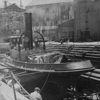 Image: A tugboat sits on stands in a dry-dock. A group of men sit facing the vessel in the foreground