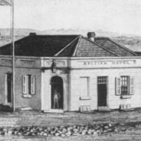 Image: A rectangular single-storey building a short distance from a riverbank. A man stands in the front doorway, while other men, including an Aboriginal man with spears, stand nearby. 