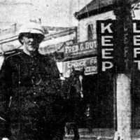 Image: A Caucasian man in an early twentieth century police uniform stands next to a marker with the words ‘Keep’ and ‘Left’ painted on it in large block letters