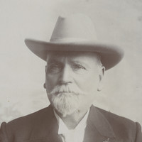 Image: A photographic portrait of an elderly Caucasian man with a white goatee. He is wearing a Stetson hat and a dark-coloured overcoat