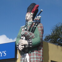 Image: large painted figure of a man in a kilt playing the bagpipes