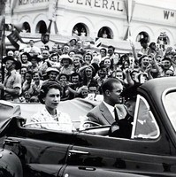 Image: Black and white photo of people in car surrounded by a crowd