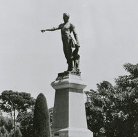 Image: A statue of a man upon a plinth surrounded by formal gardens. His arm is outstretched with his finger pointing.