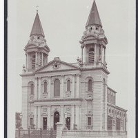 Image: A large church with twin spires, clerestory windows, and wide steps leading to a front door flanked by six decorative columns, three on either side, which are repeated on a second storey and topped by a pediment.