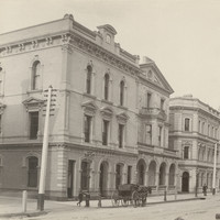 Image: A row of three storey grand stone buildings lining a dirt street.