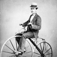Image: man in a top hat and suit riding a velocipede with wooden wheels