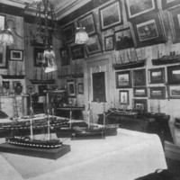Image: A small room festooned with several works of art on its walls and ship models on tables