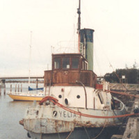 Image: A derelict tugboat is moored against a wharf. A handful of other small boats are also moored at the same wharf