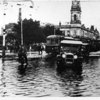 Image: View of Victoria Square showing motorcars, a motorbike rider and the electric trams navigating the flooded streets through Victoria Square in 1925
